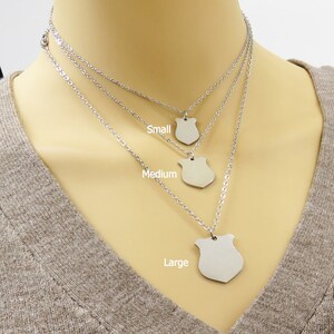 May include: Three silver necklaces with shield-shaped pendants. The necklaces are layered, with the smallest pendant labelled "Small", the middle pendant labelled "Medium", and the largest pendant labelled "Large".