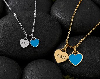 May include: Two necklaces with delicate chains, one silver-toned and one gold-toned. Each necklace features two heart-shaped charms: one solid metal heart engraved with the Greek letters Alpha Delta Pi (ΑΔΠ) and one heart with a bright blue enamel inlay.