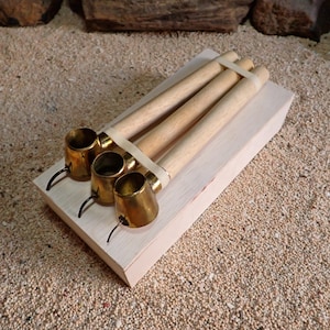 Peut inclure: Trois pipes à fumer en laiton avec des tuyaux en bois clair, maintenues ensemble par un élastique blanc, reposant sur un bloc de bois rectangulaire clair. Chaque pipe présente un foyer en laiton métallique et un embout noir fin et courbé.