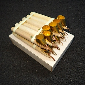 May include: A set of batik tools, including wooden handled pens with brass reservoirs and copper spouts, arranged on a small wooden block. The tools are secured with rubber bands. The image is shot from a high angle.