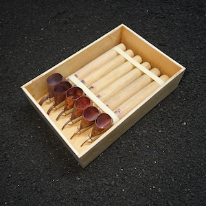 May include: A rectangular wooden box containing five identical tools, each featuring a long, cylindrical light-colored wooden handle attached to a small, conical copper-colored metal scoop at the end, secured by a light-colored wooden crossbar.