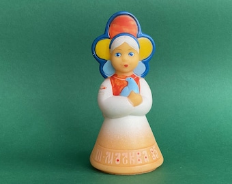 Könnte beinhalten: Eine weiße Keramikfigur eines Mädchens, das einen blauen und orangenen Hut mit gelbem Blumendesign trägt. Sie hält einen blauen Vogel in ihren Armen. Die Figur trägt den Text "III-1985" auf der Unterseite.