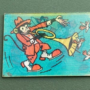 Puede incluir: Una pegatina rectangular con un personaje de dibujos animados con un atuendo y sombrero rojos tocando una trompeta amarilla. El personaje está rodeado de pequeños pájaros estilizados sobre un fondo turquesa.