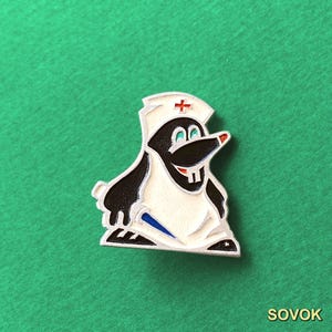 Puede incluir: Un pin de esmalte metálico que muestra un topo de dibujos animados vestido de enfermero, con una cofia blanca con una cruz roja. El topo tiene pelaje negro, un delantal blanco y dos dientes frontales prominentes. Incluye detalles azules y rojos.