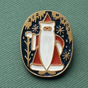 Pode incluir: Pin de Natal vintage com um design de Pai Natal. O pin oval tem uma borda dourada, um fundo azul escuro e uma figura de Pai Natal em vermelho e branco. O pin tem texto em letras cirílicas.