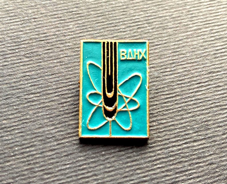 Peut inclure: Une &eacute;pingle carr&eacute;e en &eacute;mail turquoise avec une bordure dor&eacute;e. L'&eacute;pingle pr&eacute;sente un design d'atome stylis&eacute; avec une bande verticale noire et or et les lettres cyrilliques "ВДНХ" en blanc.