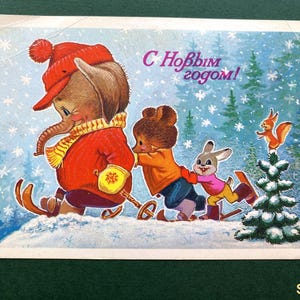 May include: A vintage-style postcard illustration featuring an elephant in a red hat and sweater, a bear, and a rabbit skiing through a snowy forest. A squirrel sits atop a small pine tree. The text C Новым годом! is printed in purple.