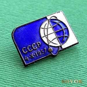 Puede incluir: Un pin rectangular de metal con un diseño de esmalte azul y blanco. El pin muestra un gráfico de un globo terráqueo con un satélite en órbita, el texto CCCP y la fecha 4-X-1957. Los bordes están delineados con un fino marco metálico.