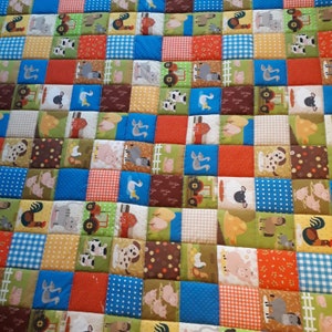 Könnte beinhalten: Ein Patchwork-Quilt mit Bauernhofthema. Der Quilt besteht aus zahlreichen Quadraten in verschiedenen Farben, darunter Rot, Blau, Grün und Braun. Jedes Quadrat zeigt ein anderes Bauernhoftier oder ein Bild mit Bezug zum Bauernhof, wie Kühe, Schweine, Traktoren und Scheunen.