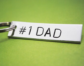 May include: A silver keyring with a white tag that says "#1 DAD" in black lettering.