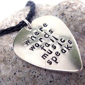 May include: Silver guitar pick necklace with a black leather cord. The pick has the words "where words fail music speaks" engraved on it.