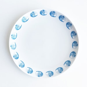 May include: A white ceramic plate with a blue and white design of dumplings around the rim.