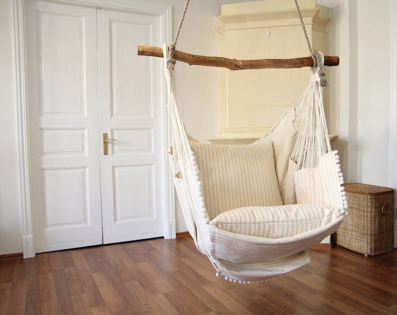 Peut inclure: Un fauteuil hamac blanc avec un cadre en bois et des coussins ray&eacute;s, suspendu dans une pi&egrave;ce avec des portes blanches et un sol en bois.