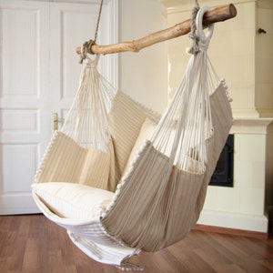 Peut inclure: Un fauteuil hamac ray&eacute; blanc et beige avec un coussin blanc. Le hamac est suspendu &agrave; une poutre en bois.