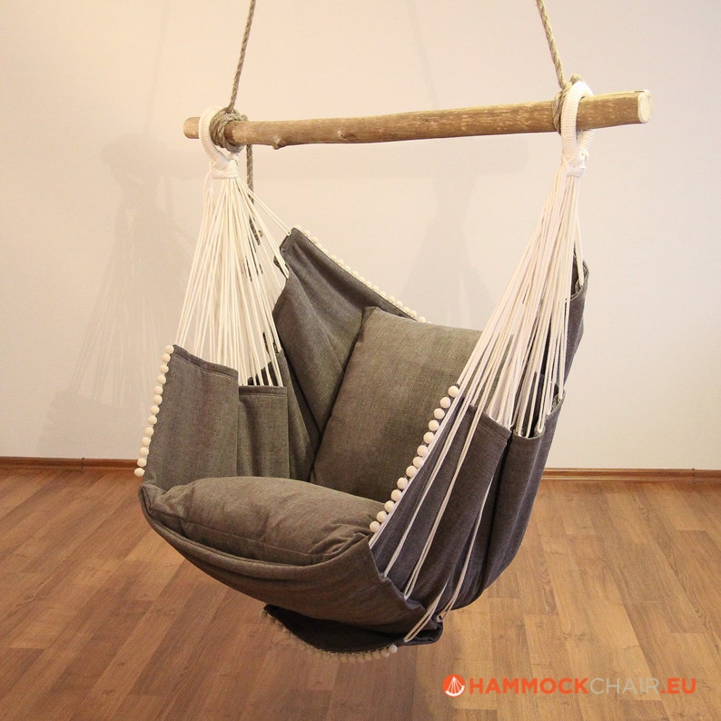 May include: A gray hammock chair with white rope and wooden dowel. The chair has a thick cushion and is hanging from the ceiling.
