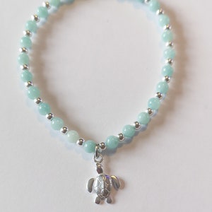 Puede incluir: Un brazalete de cuentas azul claro y plateado con un dije de tortuga plateado.