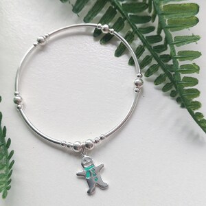 May include: A silver bracelet with a gingerbread man charm. The charm is green and white with a silver outline. The bracelet has small silver beads.