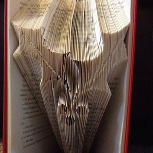 Op de afbeelding: Een boek gevouwen in de vorm van een hertenkop. Het boek heeft een rode kaft en is open om de gevouwen pagina's te laten zien.