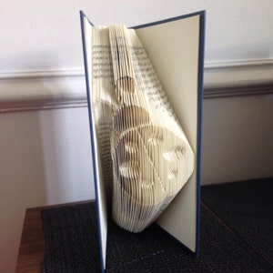 May include: A book with pages folded into a 3D sculpture of a bird. The book has a blue cover and is standing upright on a table.