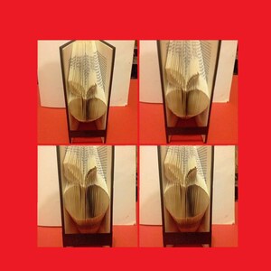 May include: A book folded into the shape of an apple, displayed on a wooden stand. The apple is made of pages from a book, and the stand is made of dark wood.