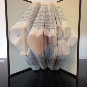Peut inclure: Une sculpture d'art de livre avec des pages pliées en forme de cœur et d'empreintes de pattes. Le livre est ouvert et les pages sont pliées pour créer un design 3D. Le livre est sur une surface noire.