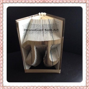 Könnte beinhalten: Eine Buchkunstskulptur des mathematischen Symbols Pi, hergestellt durch Falten der Seiten eines Buches. Das Buch ist geschlossen und steht aufrecht auf einem Tisch. Der Titel "Personalised Book Art" ist auf dem Buchrücken sichtbar.