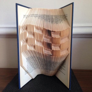 May include: A book with blue covers, its pages intricately folded to form a three-dimensional geometric design. The folded pages create a textured pattern, demonstrating the art of book folding.