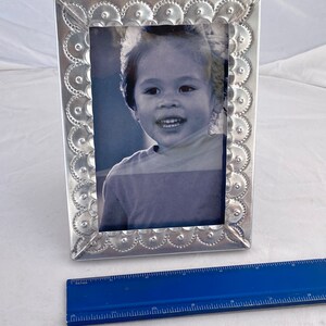 May include: A silver picture frame with a scalloped edge and a black and white photo of a child inside. The frame is about 7 inches tall.