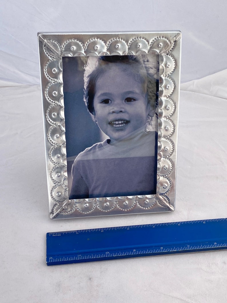 May include: A silver picture frame with a scalloped edge and a black and white photo of a child inside. The frame is about 7 inches tall.