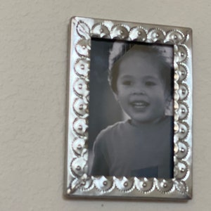 May include: A silver picture frame with a decorative border and a black and white photo of a child smiling.