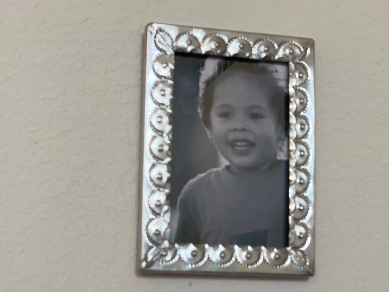 May include: A silver picture frame with a decorative border and a black and white photo of a child smiling.
