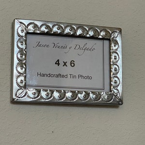 May include: A silver metal picture frame with a decorative border. The frame is labeled "Jason Yowinis y Delgado" and "4x6 Handcrafted Tin Photo".