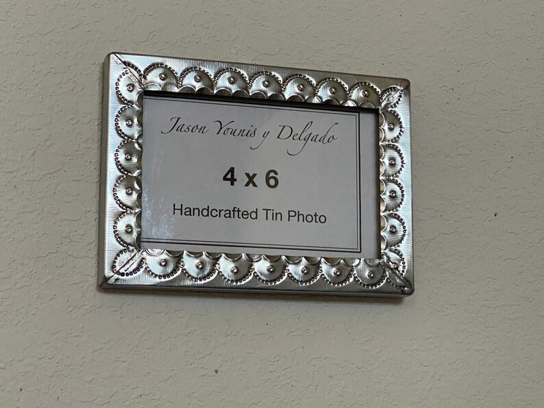 May include: A silver metal picture frame with a decorative border. The frame is labeled "Jason Yowinis y Delgado" and "4x6 Handcrafted Tin Photo".