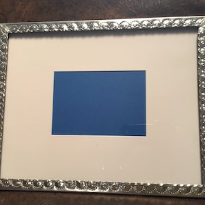 May include: A silver picture frame with a decorative embossed border. The frame has a white mat and a blue insert.