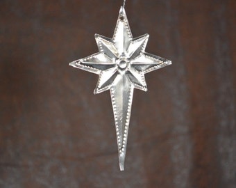 May include: A silver metal star ornament with a pointed tip and a beaded border. The star has a raised center with a circular design.