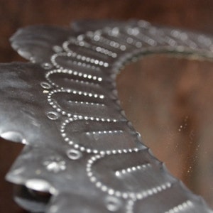 May include: A silver metal mirror with a decorative scalloped edge. The mirror has a floral design with small circles around the edge.