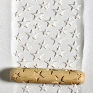 May include: A wooden rolling pin with a star pattern carved into the surface. The rolling pin is used to create star-shaped impressions in clay or dough.