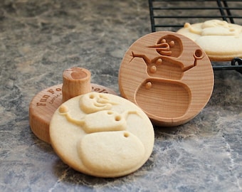 May include: Two wooden cookie cutters shaped like snowmen, one with a cookie pressed into it. The cookie cutter has the words "Fun Food" and "Cookie" on it.