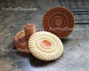 May include: Three wooden cookie cutters with intricate designs. The cutters are used to create decorative edges on cookies. The cutters are on a brown surface. FunFoodTools.com is printed on the cutters.