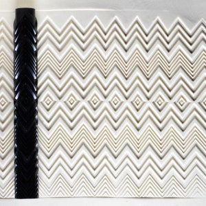 May include: A black and white textured roller with a chevron pattern. The roller is used to create a decorative pattern on a surface.