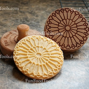 May include: Two wooden cookie cutters with a geometric design, and a cookie made with the cutter. The cookie cutters are brown and the cookie is light brown. The cookie cutters have the text "FunFoodTools.com" on them.