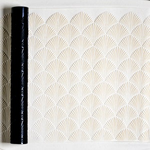 May include: A black rolling pin with a decorative fan pattern. The rolling pin is on a white surface with a matching fan pattern.