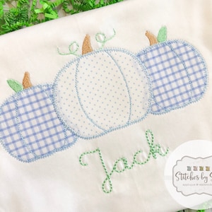 May include: A white onesie with three embroidered pumpkins in blue and white gingham patterns. The name "Jack" is embroidered in green below the pumpkins. The onesie is made by Stitches by Sara.