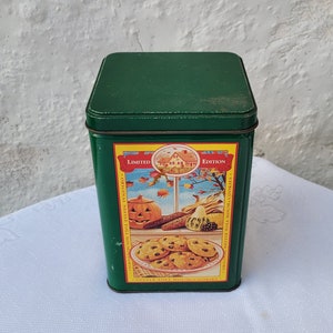 May include: A green rectangular tin with a lid, featuring a colorful autumn-themed label. The label includes a pumpkin, cookies, and the words "Limited Edition". The tin is likely for storage.