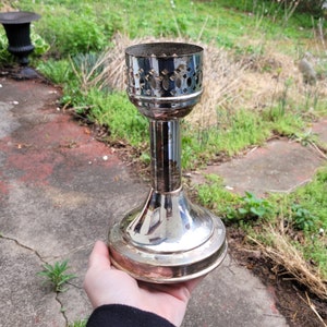 May include: A silver candle holder with a decorative design. The holder has a round base and a tall, slender stem.