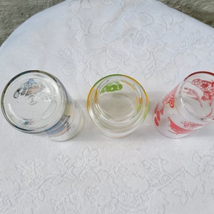 May include: Three clear glass drinking glasses with colorful designs. The glasses have a red, green, and blue design.