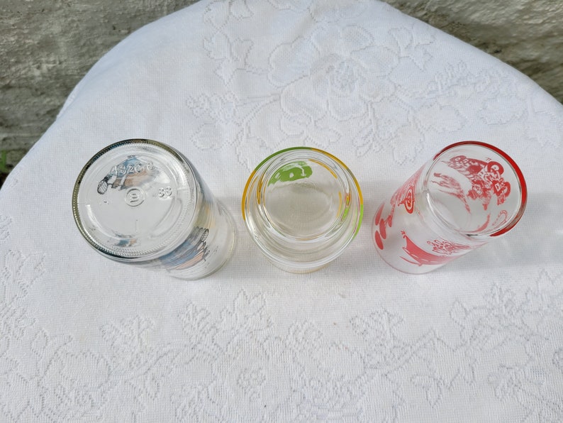May include: Three clear glass drinking glasses with colorful designs. The glasses have a red, green, and blue design.