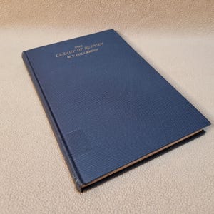 May include: A hardcover book titled "The Legacy of Bunyan" by W.Y. Fullerton. The book has a dark blue cover with gold lettering. The book is slightly angled, showing the textured cover and the edges of the pages.