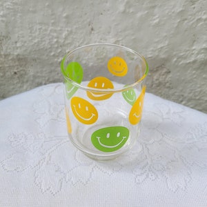 May include: A clear glass with yellow and green smiley faces printed on the side.