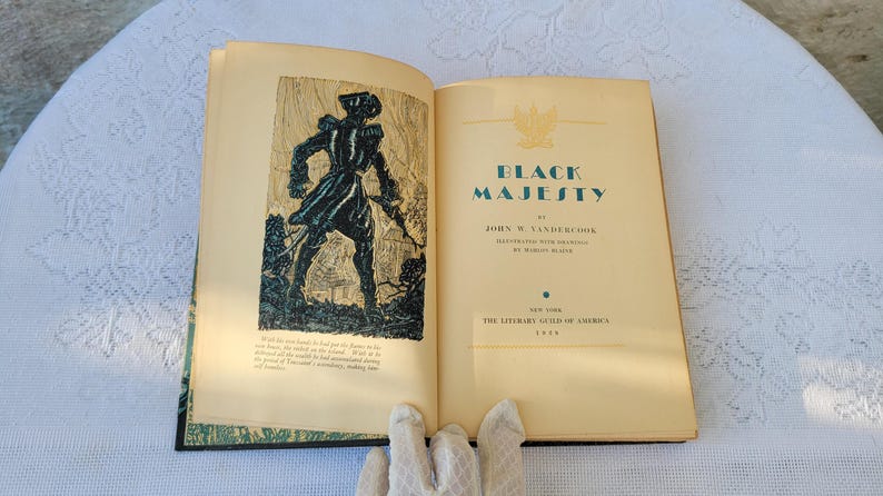 May include: An open book titled "Black Majesty" by John W. Vandercook. The book cover features a black and white illustration of a man in a military uniform standing in a forest.